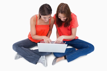 Two smiling teenagers looking at a laptop while sitting cross-leggedの写真素材
