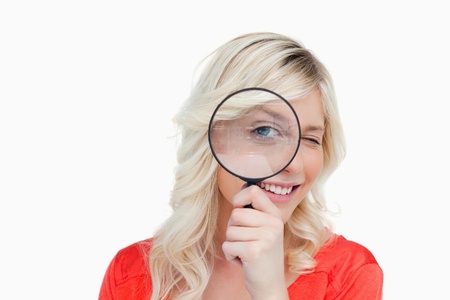 Woman looking through a magnifying glass while showing a blink of an eyeの写真素材