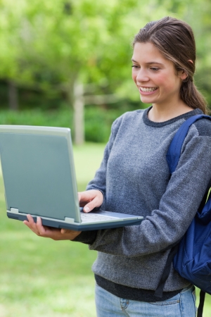 Young student looking at the screen of her laptop while smiling and standing uprightの写真素材