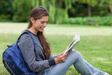 Young calm girl sitting on the grass while attentively reading a bookの写真素材