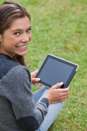 Young girl using her tablet computer while sitting on the grass and beamingの写真素材