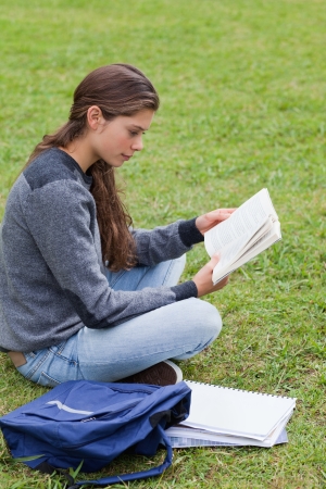 Young serious girl reading a book while sitting down with her notebook next to herの写真素材