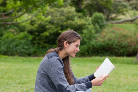 Side view of a young girl showing a great smile while reading a book on the grassの写真素材