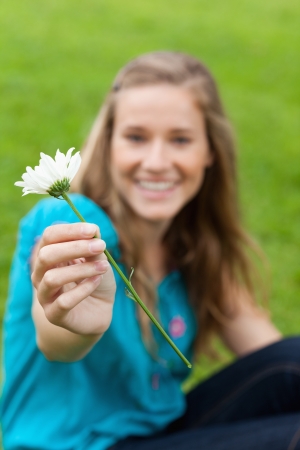 White flower held by a young smiling woman sitting in a parkの写真素材