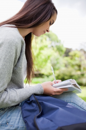 Young smiling student doing her homework while sitting in a parklandの写真素材