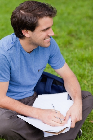 Young smiling man looking away while sitting on the grass in a park and workingの写真素材