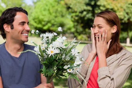 Young woman holding her hands against her face ecstatically as presented with flowers by her friend in a sunny park environmentの写真素材