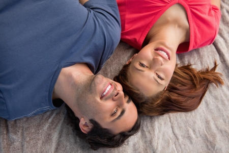 Two smiling friends lying next to each other as they look into the sky while on a grey quiltの写真素材