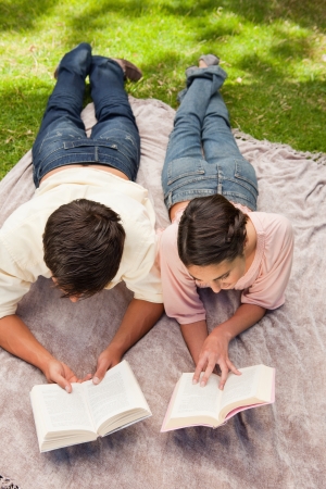 Elevated view of a man and a woman reading books while on a lying next to each other on a blanket in the grassの写真素材