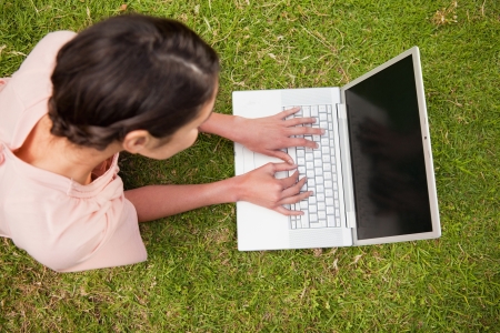 Elevated view of a woman while she uses a white laptop as she is lying prone in grassの写真素材