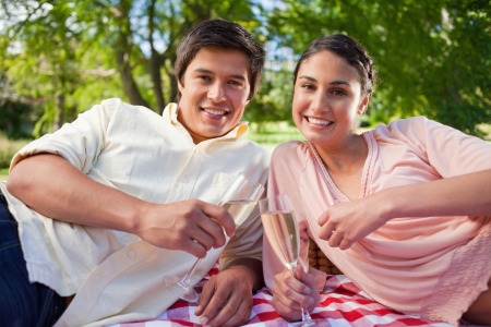 Two friends smiling as they look in front of them while holding glasses of champagne during a picnicの写真素材