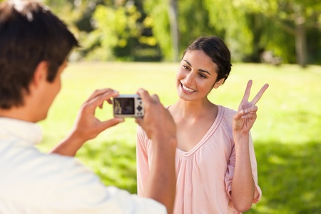 Using a camera, the man takes a photo of his friend smiling while giving the peace sign in a parkの写真素材