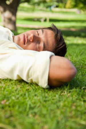 Man lying in grass with his eyes closed and his hands resting underneath the side of his headの写真素材