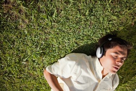 Elevated view of a man with his eyes closed while using headphones to listen to music as he lies down on the grassの写真素材