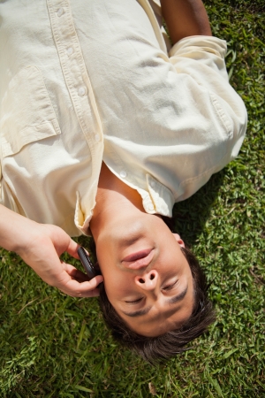 Man with his eyes closed using a mobile phone as he lies down on the grassの写真素材