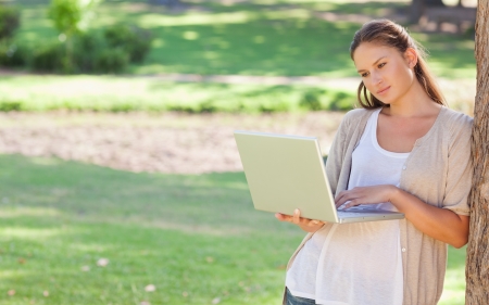 Young woman leaning against a tree while using a laptopの写真素材