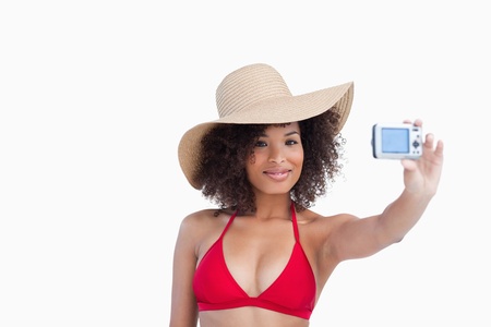 Smiling woman in beachwear photographing herself against a white backgroundの写真素材
