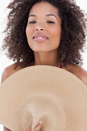 Attractive brunette woman hiding her body behind a hat against a white backgroundの写真素材
