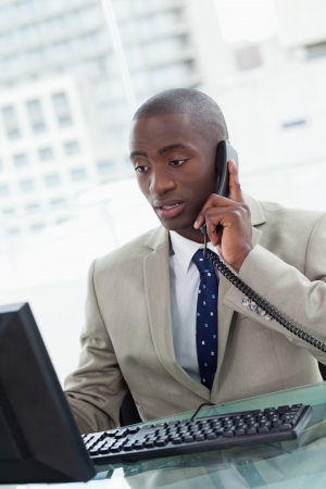 Portrait of a focused office worker making a phone call while using a computerの写真素材
