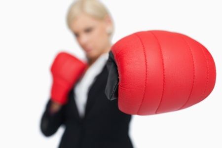 Blonde businesswoman with red boxing gloves fighting against white backgroundの写真素材