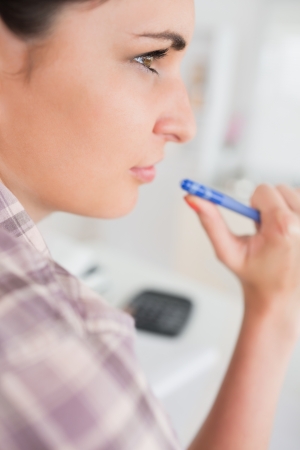 Thoughtful woman holding a pen in a living roomの写真素材