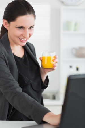 Woman holding a juice glass while looking at a laptop in a living roomの写真素材