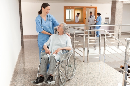 Nurse watching over old women sitting in wheelchair in hallwayの写真素材