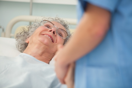 Elderly female patient looking up at nurse from hospital bedの写真素材