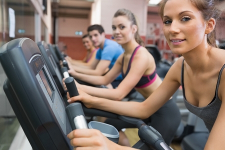 Four people smiling and riding on an exercise bike in gymの写真素材