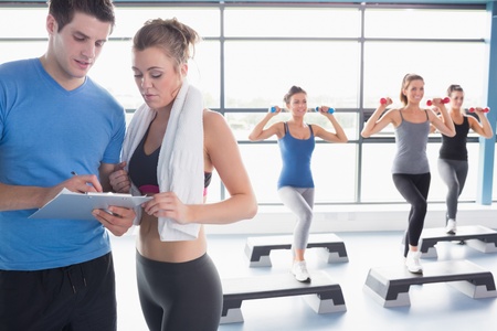 Women doing aerobics while trainer talking to woman in gym