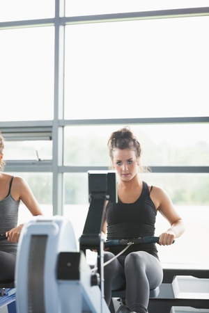 Two women training on row machines in a gym