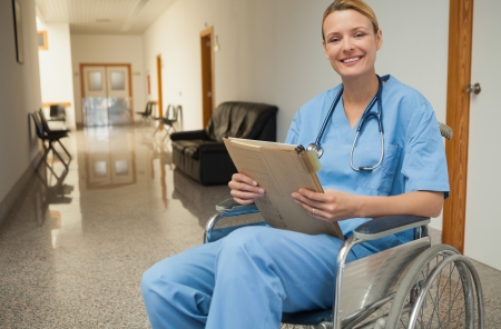 Smiling nurse in a wheelchair holding a folder in hospital corridorの写真素材