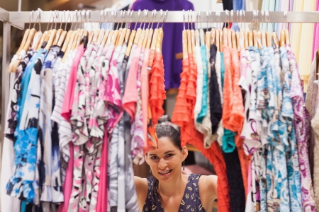 Woman standing behind a clothes rack of a store smiling の写真素材