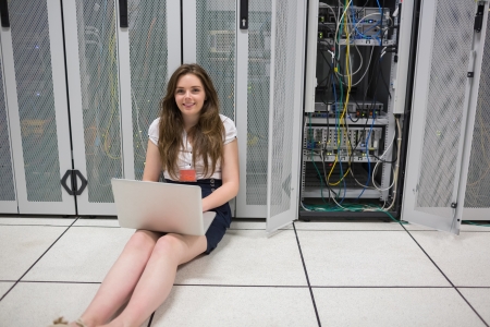Woman checking the servers with laptop sitting on the floor in data centerの写真素材