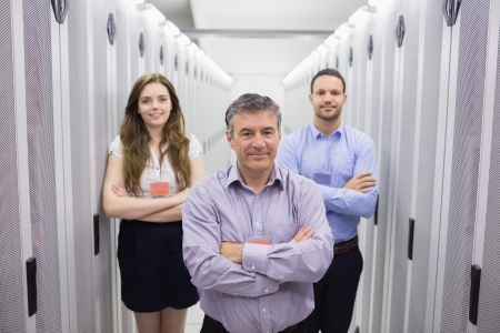 Three smiling people standing in data center with arms crossed Three smiling people standing in data center with arms crossed