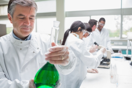 Chemist viewing liquid while other persons doing research in the laboratoryの写真素材