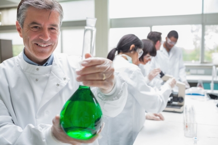 Chemist smiling and holding beaker of green liquid in labの写真素材
