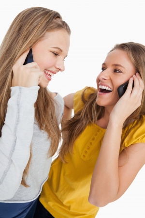 Close-up of two beautiful students laughing on the phone against white backgroundの写真素材