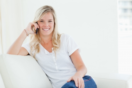 A smiling woman talking on her phone while looking at the camera as she sits on the couch の写真素材