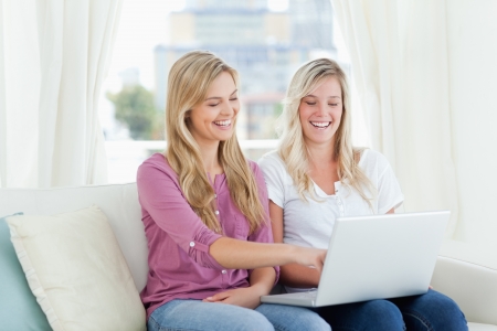 Two women laughing together as they look at something on the laptop in their hands の写真素材