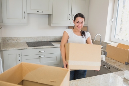 Young woman unpacking in kitchen holding box