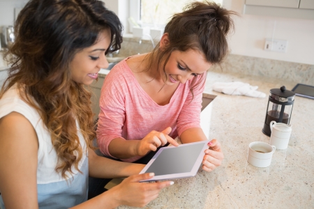 Happy friends looking at tablet computer and having coffee in kitchenの写真素材