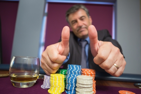 Man giving thumbs up sitting at roulette table in casinoの写真素材