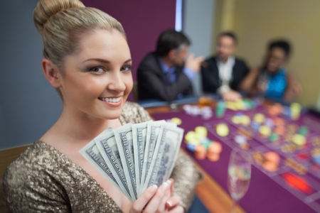 Blonde woman holding fan of dollars in casinoの写真素材