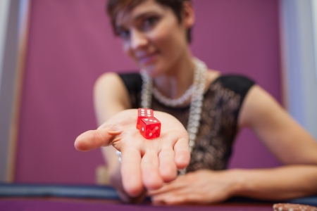 Woman sitting at table in a casino holding dices and smilingの写真素材
