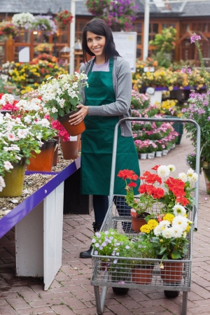 Woman filling the trolley with plants while smiling in the garden centerの写真素材
