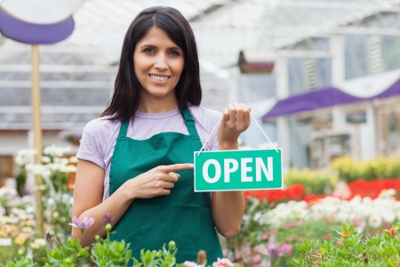 Woman in garden center pointing at the open-sign while smilingの写真素材