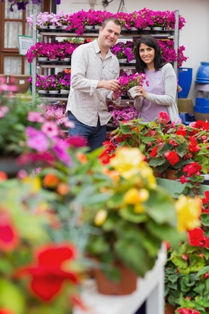 Happy couple holding pot of purple flowers in garden centerの写真素材