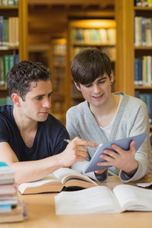 Smiling student showing another something on tablet pc studying in the libraryの写真素材