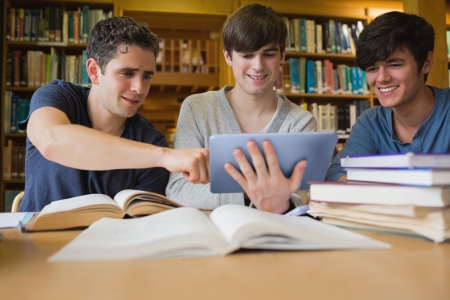 Young man pointing something out on tablet pc with others in the college libraryの写真素材